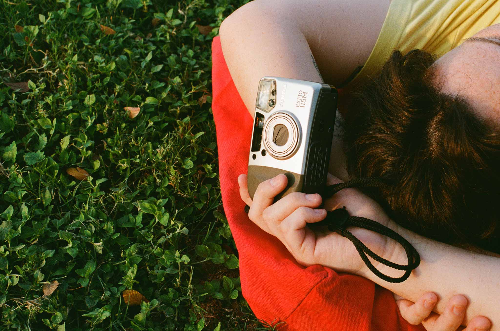 Woman holding camera while sitting on grass.